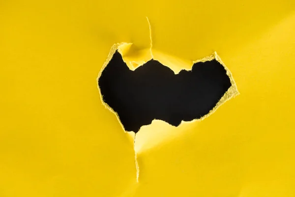 Close-up shot of hole in yellow paper isolated on black — Stock Photo