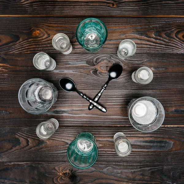 Top view of circle with different sized glasses with water and spoons on wooden table — Stock Photo