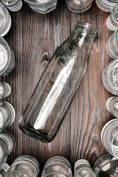 Vue du dessus de la bouteille en verre entre les verres avec de l'eau sur une table en bois — Photo de stock