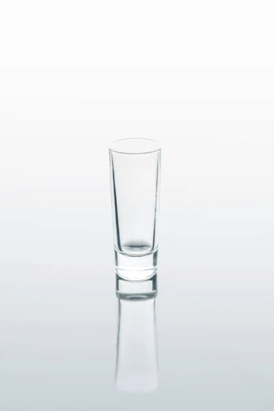 Un pequeño vaso sobre una superficie blanca reflectante - foto de stock