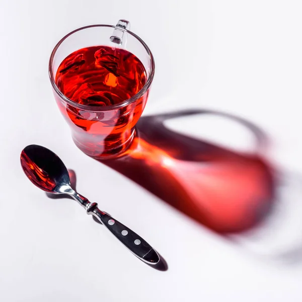 Vista ad angolo alto di tazza di vetro con tè ibisco e cucchiaio su tavolo bianco — Foto stock