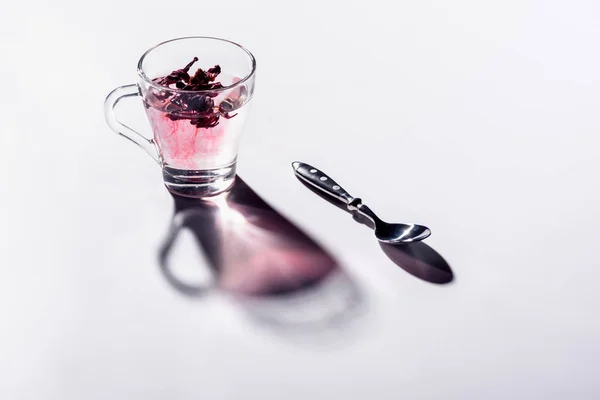 Glass cup of hibiscus tea with spoon on white table — Stock Photo