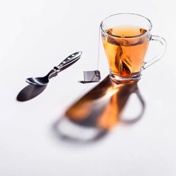 Tasse en verre de thé noir et cuillère sur la table — Photo de stock