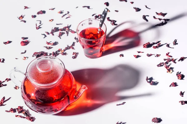 Vista de ángulo alto de la tetera de vidrio con té de hibisco y taza con cuchara en la mesa - foto de stock