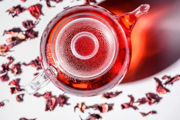 Draufsicht auf transparente Glasteekanne mit Hibiskustee und verstreutem Tee auf dem Tisch — Stockfoto