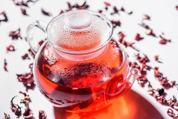 Transparent glass teapot with hibiscus tea and scattered tea on table — Stock Photo