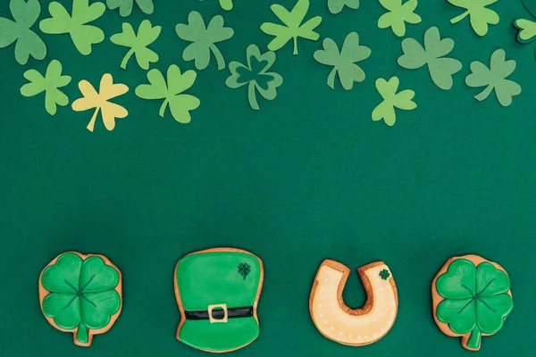 Top view of icing cookies and paper shamrock isolated on green, st patricks day concept — Stock Photo