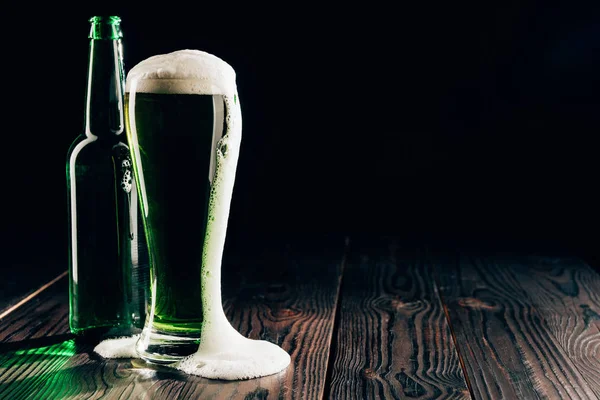 Vidro e garrafa de cerveja verde com espuma na mesa, st patricks conceito dia — Fotografia de Stock