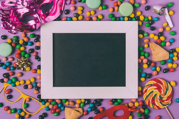 Top view of arranged masquerade masks, candies, cookies and empty blackboard isolated on purple — Stock Photo