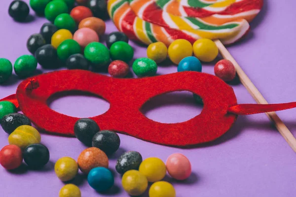 Vue rapprochée de bonbons et masque de mascarade isolé sur violet — Photo de stock