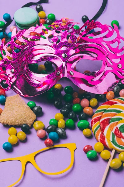 Primer plano vista de máscaras de mascarada y caramelos aislados en púrpura - foto de stock