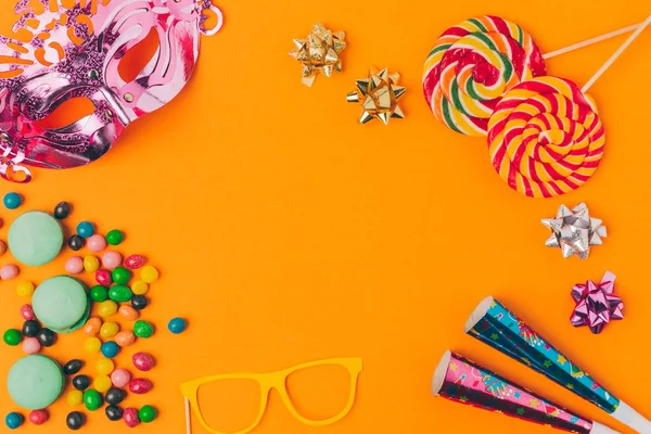 Plano con caramelos y objetos de fiesta aislados en naranja, concepto de vacaciones purim - foto de stock