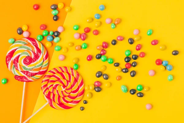 Vista superior de pirulitos e vários doces no fundo amarelo e laranja — Fotografia de Stock