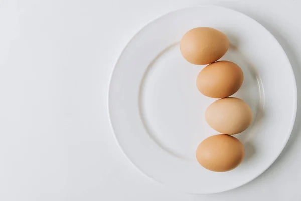 Uova marroni che depongono su piastra bianca su sfondo bianco — Foto stock