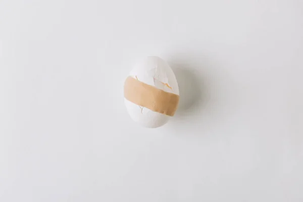 Broken white egg with medical plaster laying on white background — Stock Photo