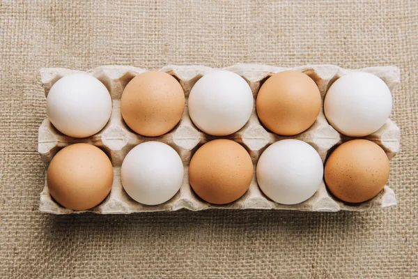 White and brown eggs laying in egg carton on sackcloth — Stock Photo