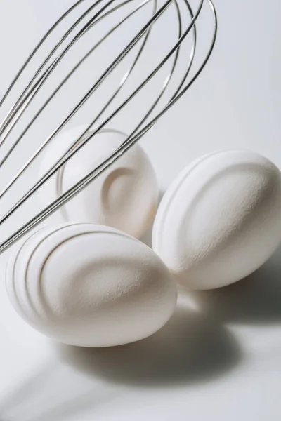 White eggs laying under whisk on white background — Stock Photo