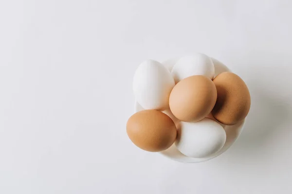 Vista superior de huevos blancos y marrones que ponen en plato blanco sobre fondo blanco - foto de stock