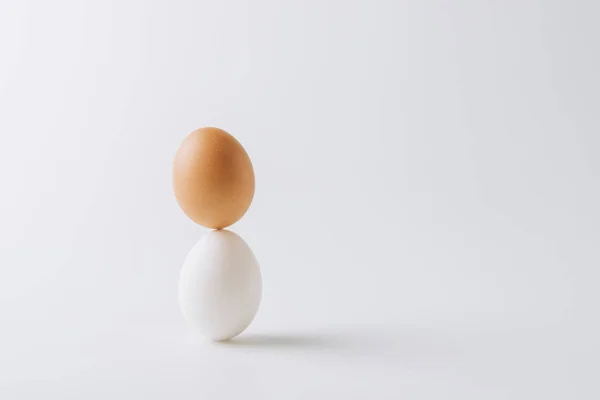 One white and one brown eggs stacked on white background — Stock Photo