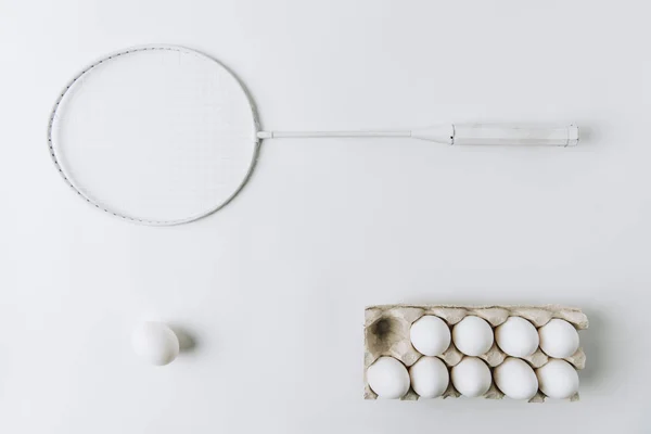 Ovo branco sobre fundo branco com outros ovos brancos em caixa e raquete — Fotografia de Stock