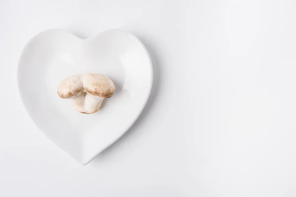 Setas crudas colocadas en placa en forma de corazón sobre fondo blanco - foto de stock