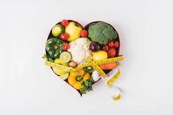 Verdure e frutta posa in piatto a forma di cuore vicino stetoscopio e nastro di misura isolato su sfondo bianco — Foto stock