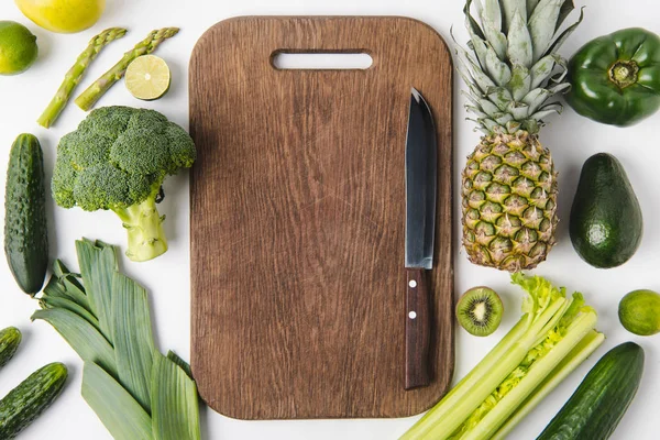 Cuchillo sobre tabla de cortar de madera con verduras verdes y frutas aisladas sobre fondo blanco - foto de stock