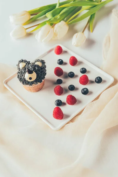 Primo piano vista di dolce muffin gustoso a forma di orso, lamponi freschi e fiori di tulipano — Foto stock