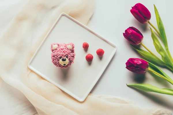 Vista dall'alto del dolce muffin gustoso a forma di orso, lamponi freschi e fiori di tulipano — Foto stock
