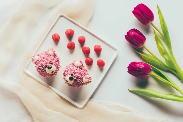 Top view of sweet tasty muffins in shape of bears, fresh raspberries and tulip flowers — Stock Photo