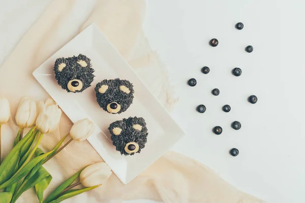 Vista dall'alto di cupcake gourmet a forma di orsi, mirtilli freschi e fiori di tulipano — Foto stock