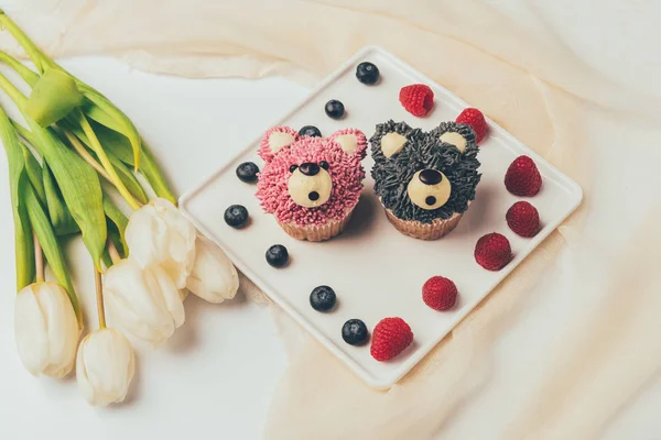 Nahaufnahme köstlicher Muffins in Form von Bären, frischen Beeren und Tulpenblüten — Stockfoto