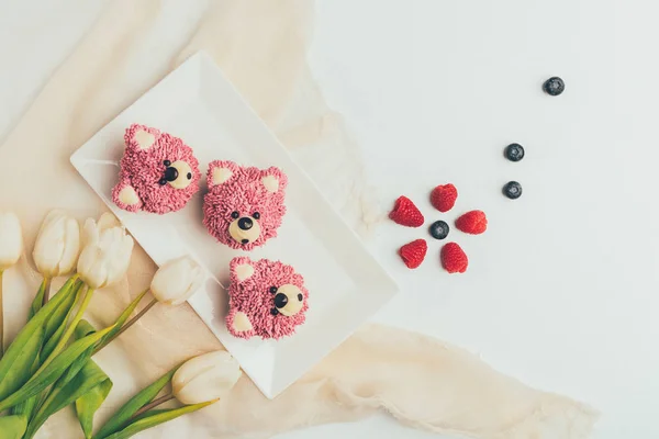 Blick von oben auf köstliche Muffins in Form von Bären, frischen Beeren und Tulpenblüten — Stockfoto