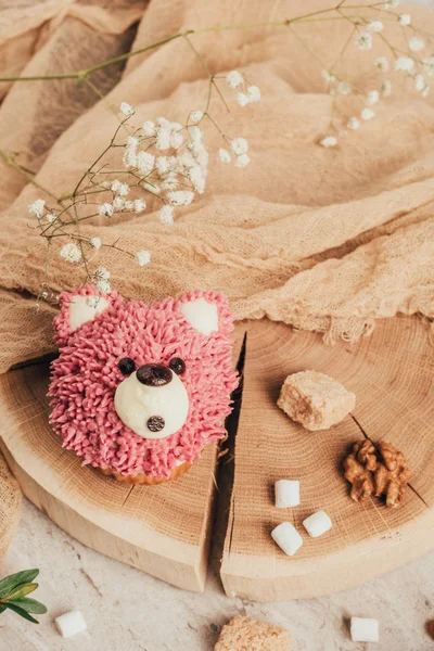 Вид сверху на сладкий розовый кекс в форме медведя и орехов с сахаром на деревянной доске — стоковое фото