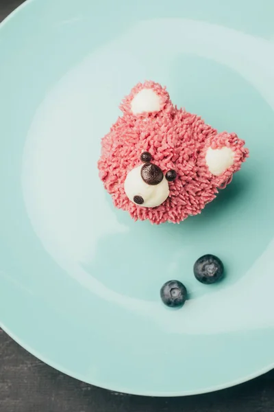 Вид зверху солодкий рожевий кекс у формі ведмедя та свіжої чорниці на блакитній тарілці — стокове фото