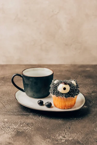 Sweet tasty blueberry muffin in shape of bear and black mug on plate — Stock Photo
