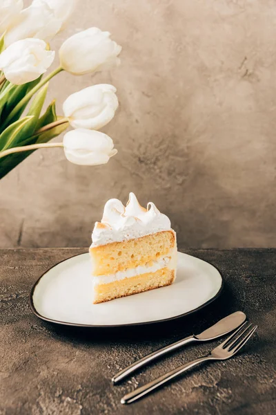 Close-up view of delicious piece of cake with whipped cream and beautiful white tulips — Stock Photo