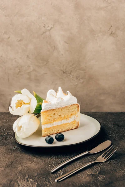 Delicioso pedaço de bolo com chantilly, mirtilos frescos e tulipas no prato — Fotografia de Stock