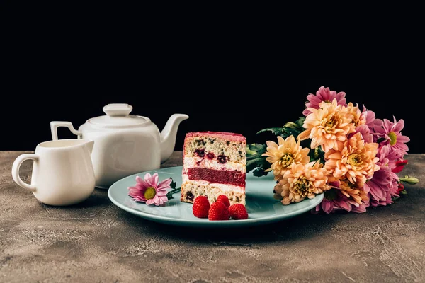 Delicioso pedazo de pastel con frambuesas, hermosas flores y hervidor de agua con jarra de porcelana - foto de stock