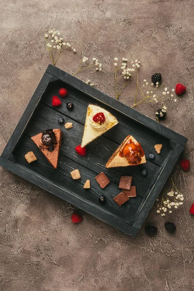 Top view of pieces of delicious cakes with chocolate and berries on wooden tray — Stock Photo