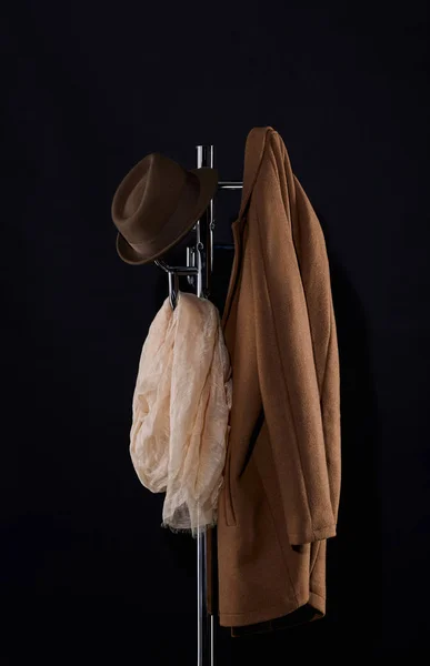 Класичне пальто, капелюх і шарф, що звисають на стелажі для пальто ізольовані на чорному — стокове фото