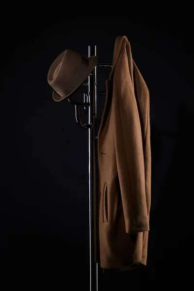 Chapéu e jaqueta clássica pendurados no rack do casaco isolado no preto — Fotografia de Stock