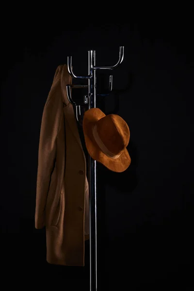Hat and coat hanging on coat rack isolated on black — Stock Photo