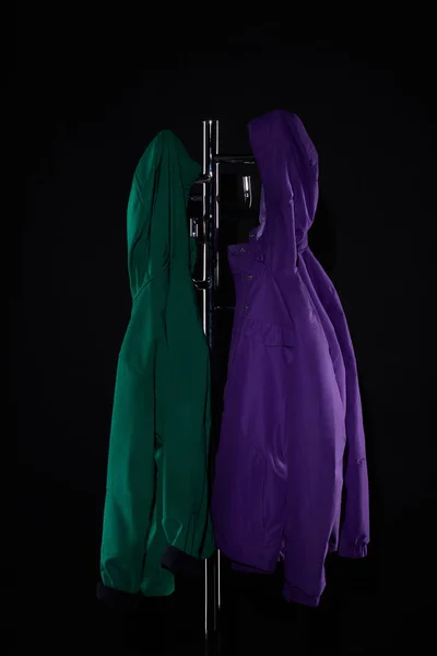 Raincoats hanging on coat rack isolated on black — Stock Photo