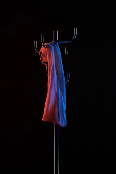 Cloth hanging on coat rack under toned light isolated on black — Stock Photo