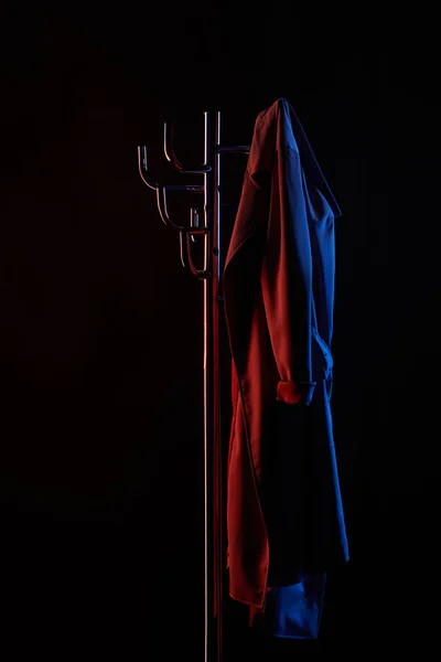 Coat hanging on coat rack under toned light isolated on black — Stock Photo