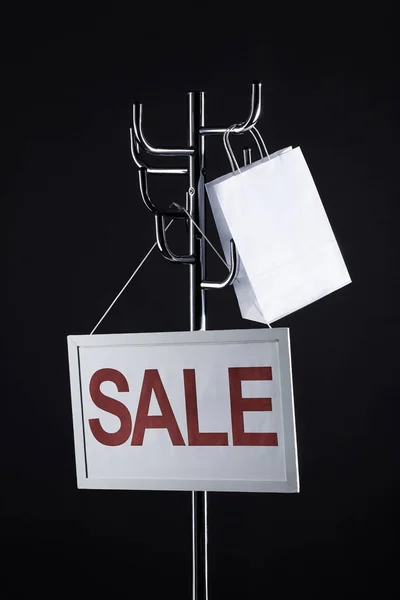 Sale signboard and paper bag on coat rack isolated on black — Stock Photo