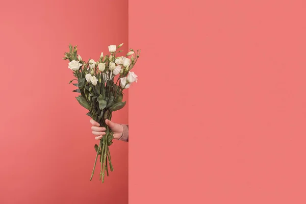 Woman sticking out white eustoma bouquet behind wall on red — Stock Photo