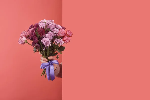 Woman sticking out flowers bouquet behind wall on red — Stock Photo