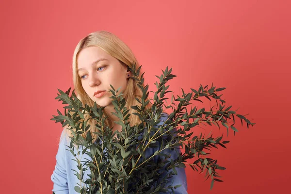 Jeune femme réfléchie avec un tas de branches d'eucalyptus isolé sur rouge — Photo de stock